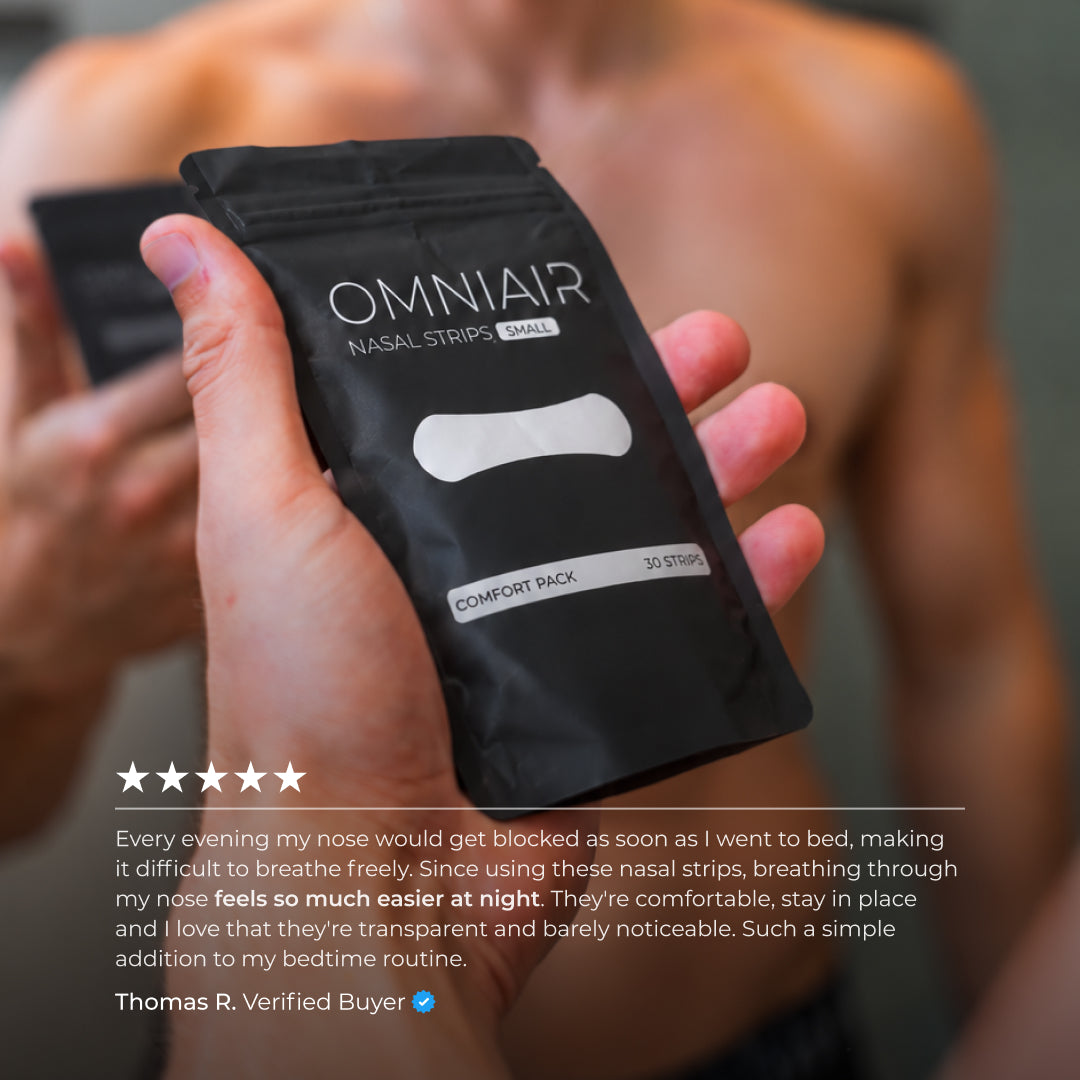 Close-up of OMNIAIR Small Transparent Nasal Strips packaging, held in front of a mirror, with a customer review highlighting easier nasal breathing at night, relief from nighttime nasal congestion, and a discreet, comfortable fit.